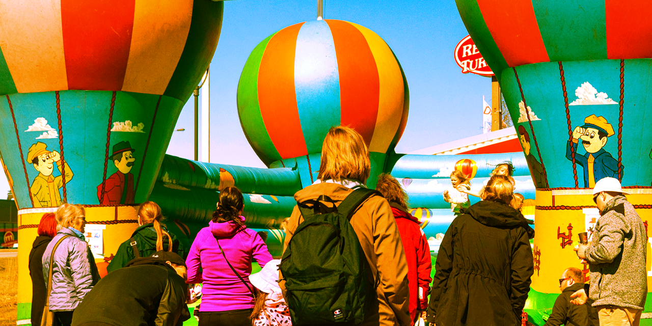 Kevättuuletuksesta otettu kuva, jossa taustalla lapsia hyppimässä värikkäässä pomppulinnassa. Edustalla aikuisia valvomassa selkä kameraan päin.