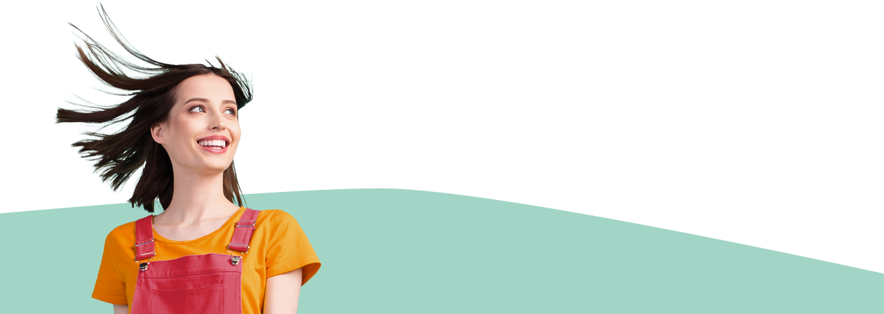 Rintakuva nuoresta naisesta nauramassa tukka tuulenpuuskasta hulmuten yllään oranssi t-paita ja punaiset haalarit.